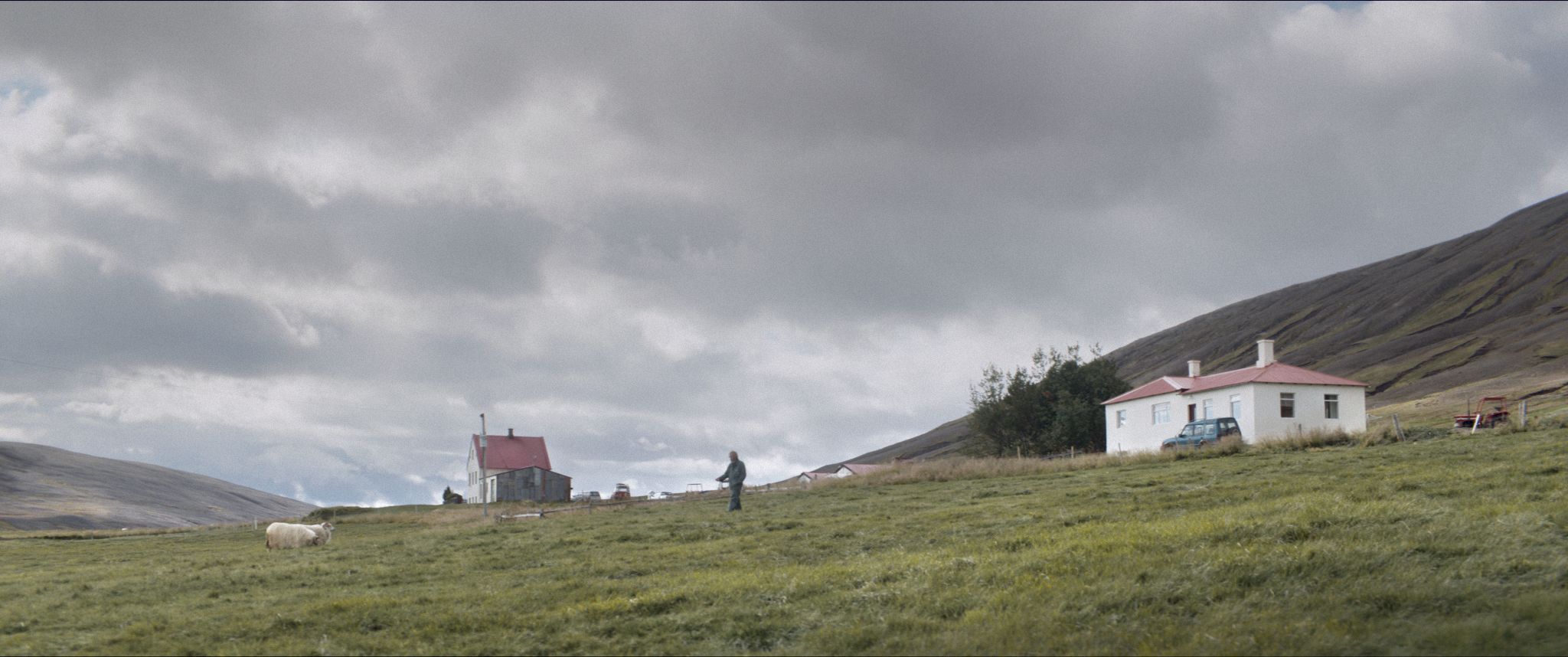 bohater na tle dwóch domów usytuowanych na odludziu - pośród rozległych, górzystych terenów Islandii